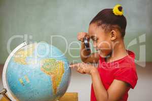 Little girl looking at globe through magnifying glass