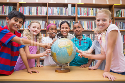 Cute pupils and teacher looking at globe in library