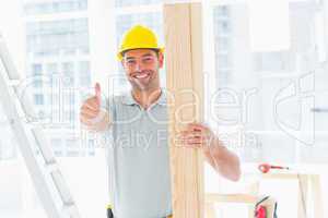 Carpenter holding plank while gesturing thumbs up in building