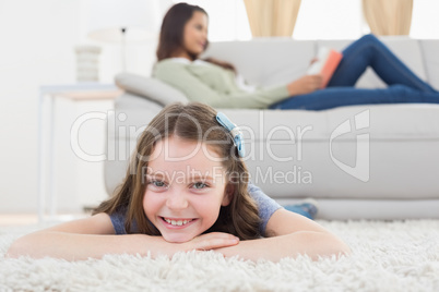 Girl lying on rug while mother relaxing at home