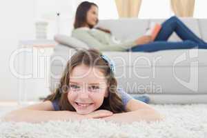 Girl lying on rug while mother relaxing at home