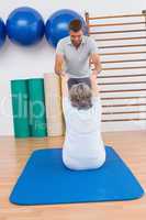 Trainer working with senior woman on exercise mat