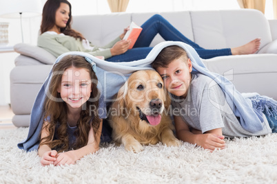 Happy siblings with dog under blanket