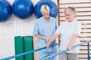 Senior woman walking with parallel bars with therapist