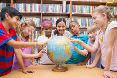 Cute pupils and teacher looking at globe in library