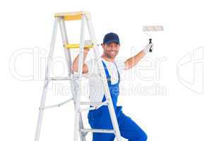 Happy handyman on ladder while using paint roller