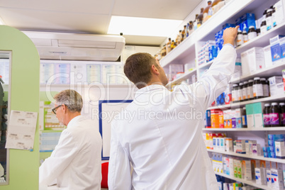 Pharmacist in lab coat taking jar from shelf