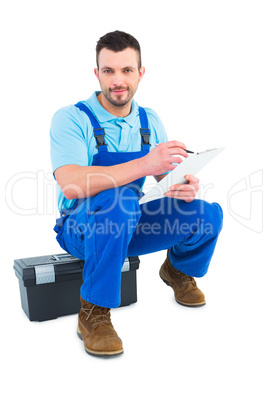 Plumber writing on clipboard while sitting on toolbox