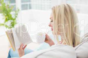 Woman reading book while having coffee on sofa