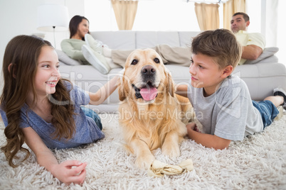 Siblings stroking dog on rug while parents relaxing on sofa