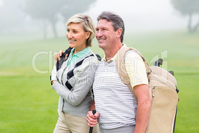 Golfing couple smiling and holding clubs