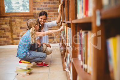 Teacher and little girl selecting book in library