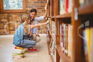 Teacher and little girl selecting book in library