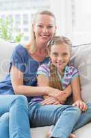 Smiling mother and daughter sitting together on sofa at home