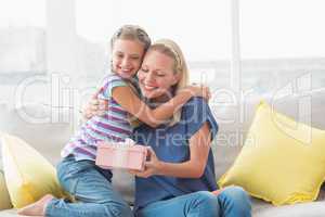 Happy mother with gift embracing daughter in house