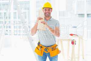 Smiling handyman carrying planks in building