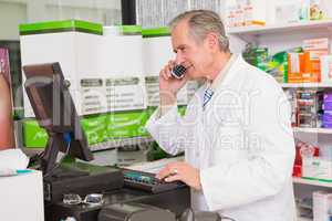 Senior pharmacist phoning while using computer