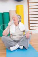Senior woman drinking water on exercise mat