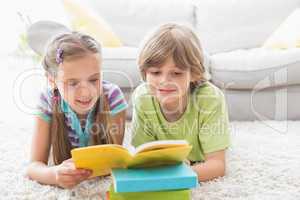 Siblings reading book while lying on rug