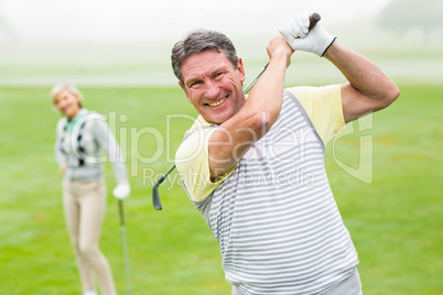 Happy golfer teeing off with partner behind him