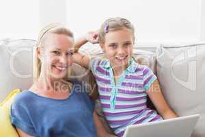 Happy girl with mother using laptop on sofa at home