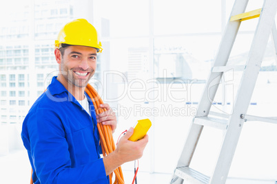 Smiling male electrician holding multimeter in office