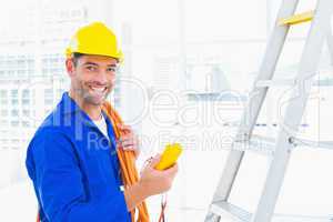 Smiling male electrician holding multimeter in office