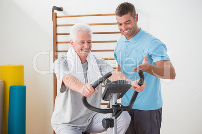 Senior man doing exercise bike with his trainer