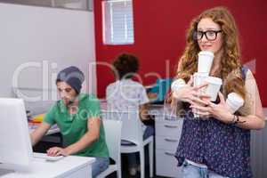 Casual businesswoman carrying disposables glasses in office