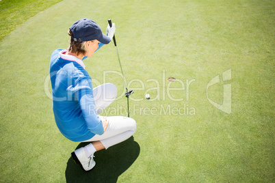 Focused lady golfer kneeling on the putting green