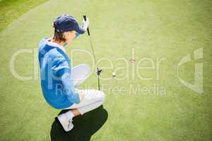 Focused lady golfer kneeling on the putting green