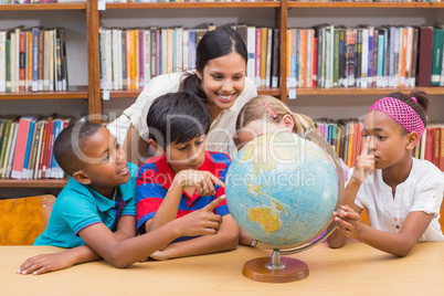 Cute pupils and teacher looking at globe in library