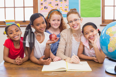 Cute pupils and teacher smiling at camera in classroom