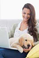 Woman with dog using laptop on sofa