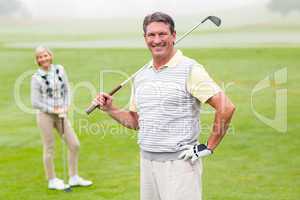 Happy golfer teeing off with partner behind him
