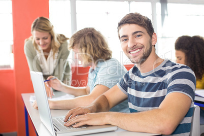 Smiling male student using laptop in classroom