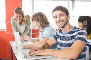 Smiling male student using laptop in classroom