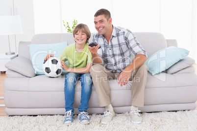 Father and son watching soccer match on sofa