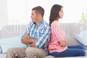 Angry couple with arms crossed sitting on sofa