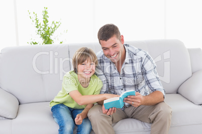 Father and son with story book sitting on sofa