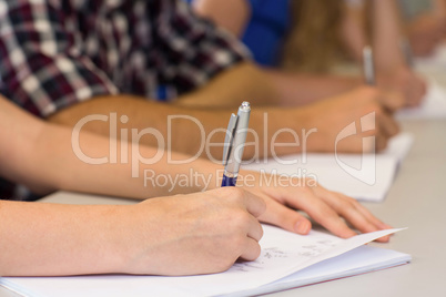 Mid section of students writing notes in classroom