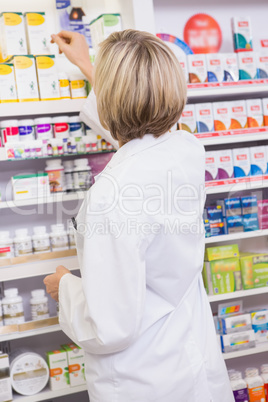 Blonde pharmacist taking medicine from shelf