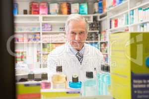 Smiling senior pharmacist standing behind a shelf