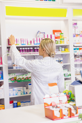 Junior pharmacist taking medicine from shelf