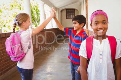 Schoolgirl with friends high fiving in background at school corr
