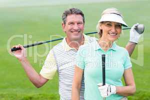 Golfing couple smiling at camera holding clubs