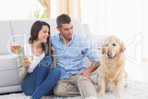 Couple holding wine glasses while looking at dog