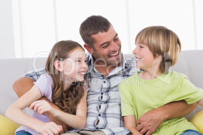 Father tickling son and daughter while sitting on sofa