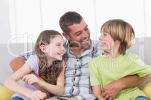 Father tickling son and daughter while sitting on sofa