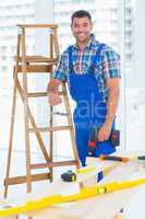 Carpenter with power drill standing by ladder at construction si